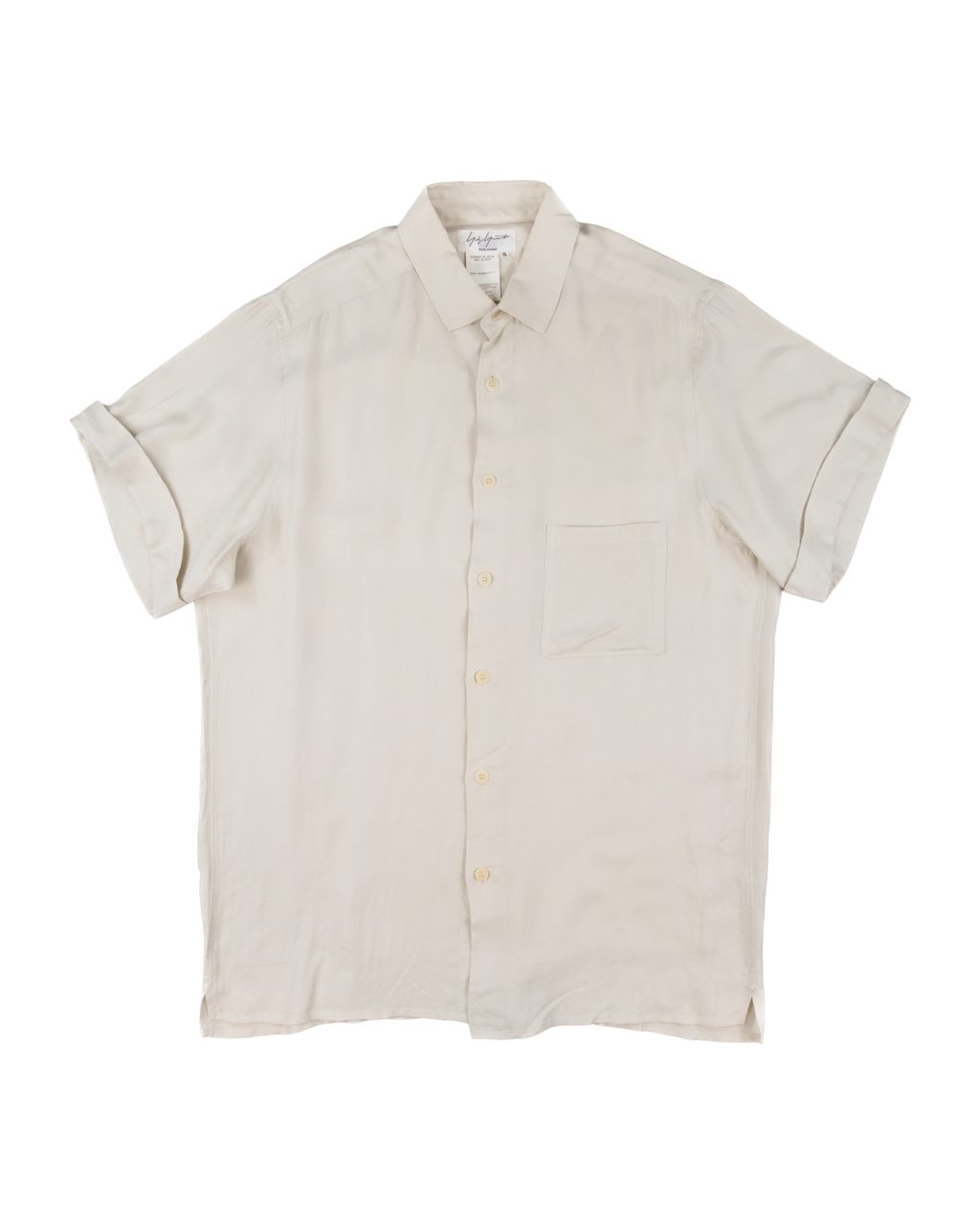 Beige short-sleeve shirt on a white background. Yohji Yamamoto off-white cream short-sleeve button-up shirt; smooth lightweight silk or rayon-like fabric with soft drape and minimalist tailoring; single chest pocket and tonal buttons; relaxed silhouette reflecting Japanese artisanal craftsmanship and understated avant-garde luxury typical of Yamamoto’s timeless design ethos.