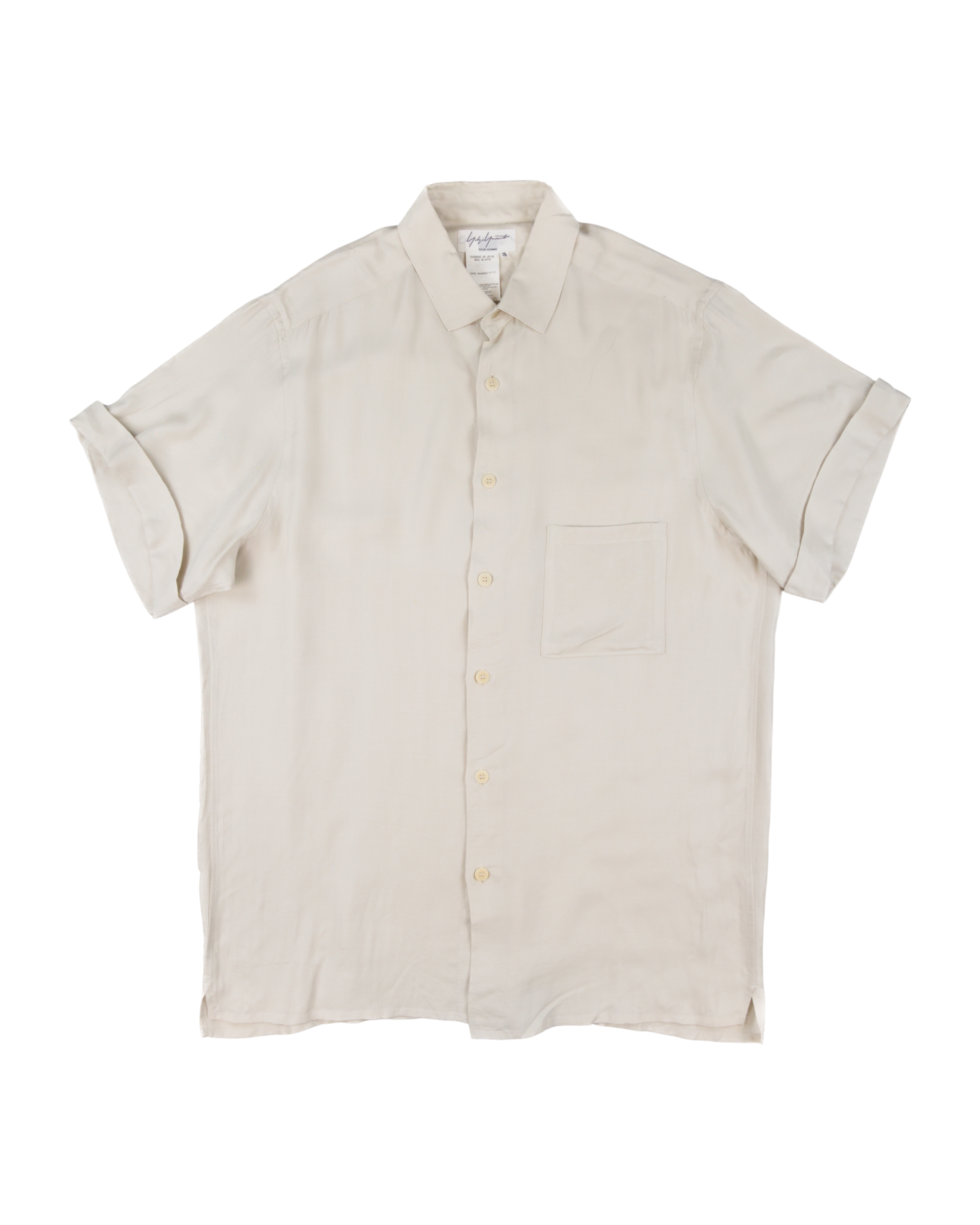 Beige short-sleeve shirt on a white background. Yohji Yamamoto off-white cream short-sleeve button-up shirt; smooth lightweight silk or rayon-like fabric with soft drape and minimalist tailoring; single chest pocket and tonal buttons; relaxed silhouette reflecting Japanese artisanal craftsmanship and understated avant-garde luxury typical of Yamamoto’s timeless design ethos.