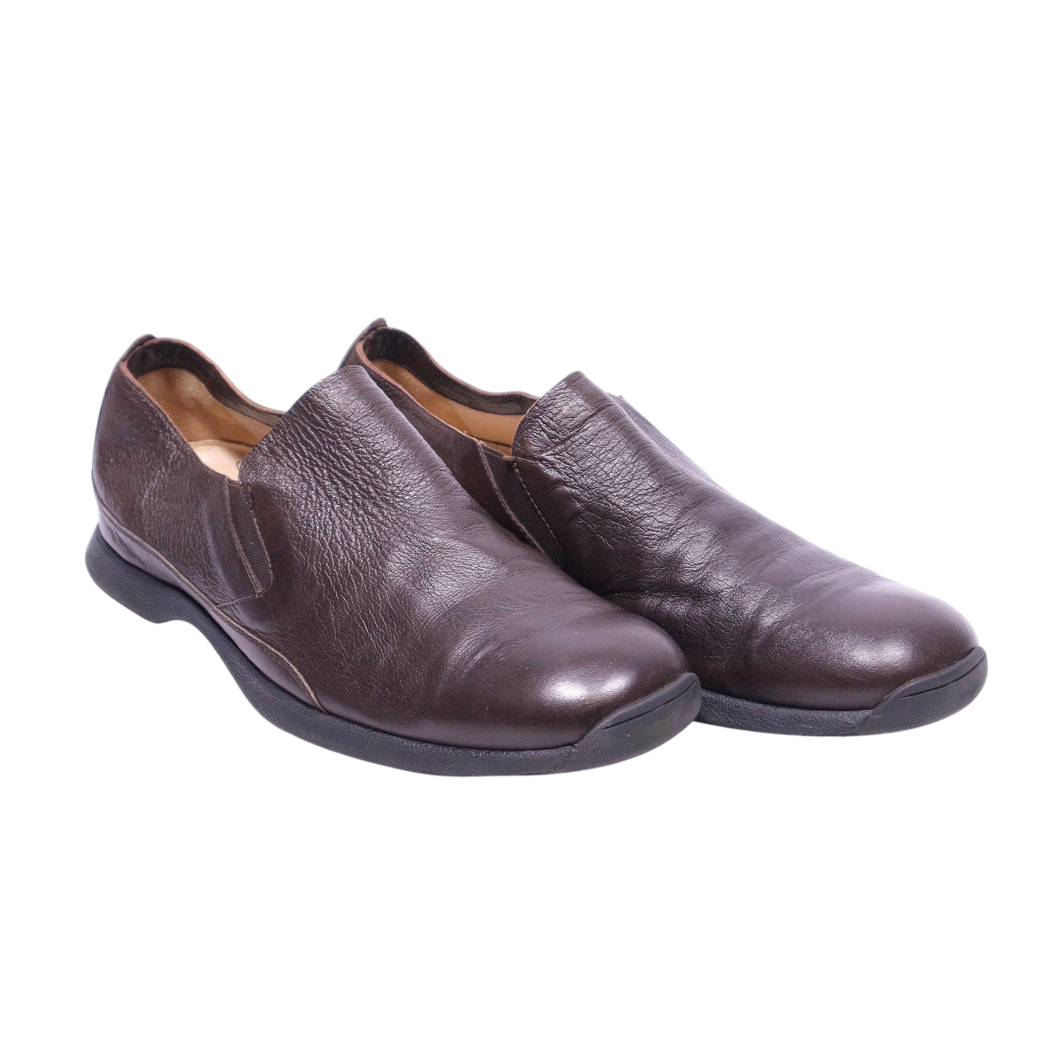 This image displays a pair of Costume National brown leather loafers. The shoes feature a sleek, slip-on design with subtle stitching details and a soft brown hue that conveys both elegance and comfort.Dark brown leather slip-on loafers with a notched vamp, rounded almond toe and low rubber sole. Minimal Italian profile with subtle grain; vintage designer, rare.