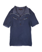 Blue polo shirt with white trim on a white background. Roberto Cavalli navy/ink-blue linen-cotton polo shirt; open half-placket and soft spread knit collar; contrast western piping with arrow appliqués at chest; short sleeves with elastic hems; lightweight summer knit; slim/regular fit, unisex casual; Y2K/western vibe; Italian luxury house craftsmanship, rare vintage.