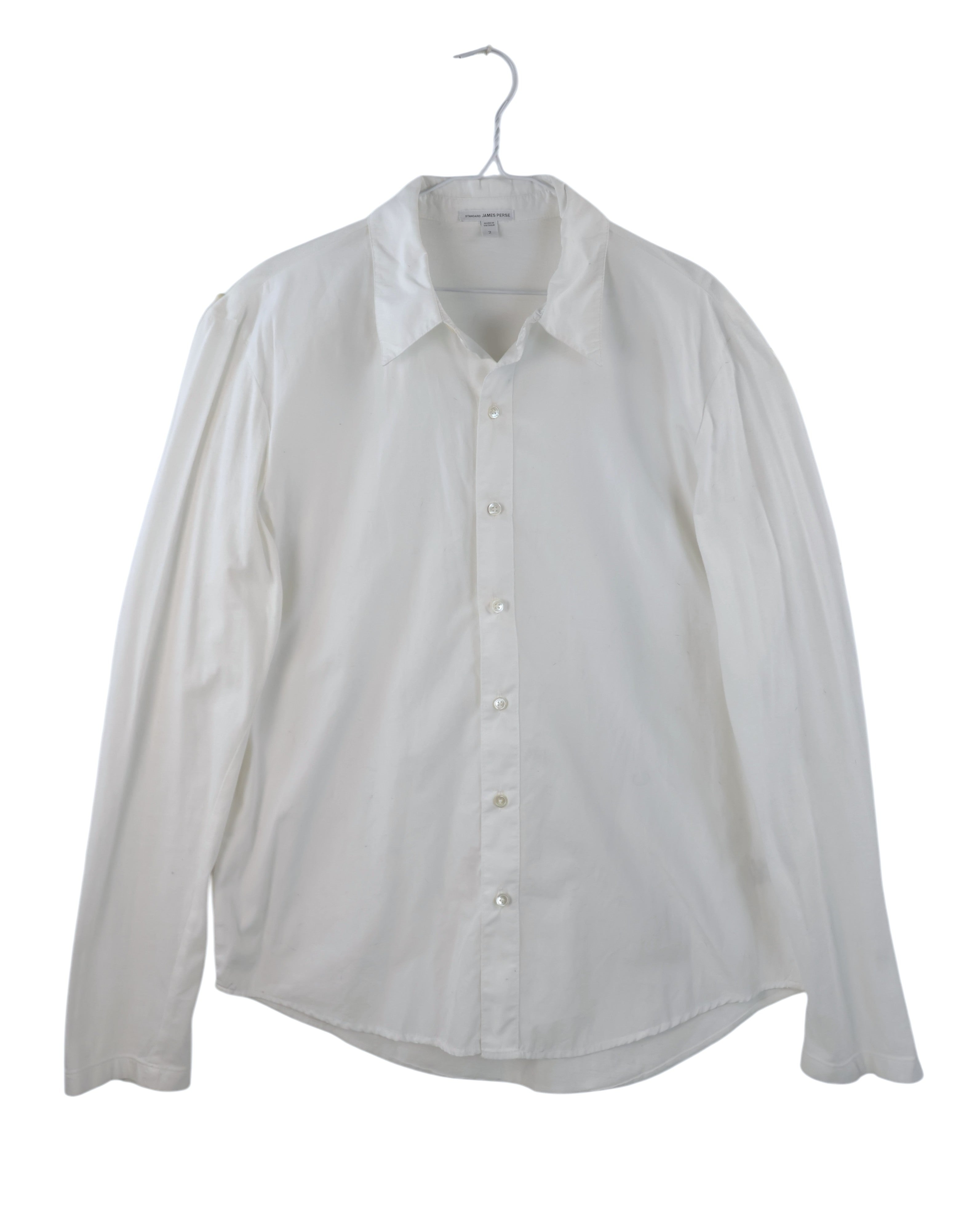 White shirt on a hanger against a white background. James Perse crisp white long-sleeve button-up shirt; smooth lightweight cotton fabric with pointed collar and minimalist tailoring; slightly relaxed fit for effortless sophistication; versatile wardrobe essential reflecting California luxury craftsmanship and timeless modern refinement for casual or dressed looks.