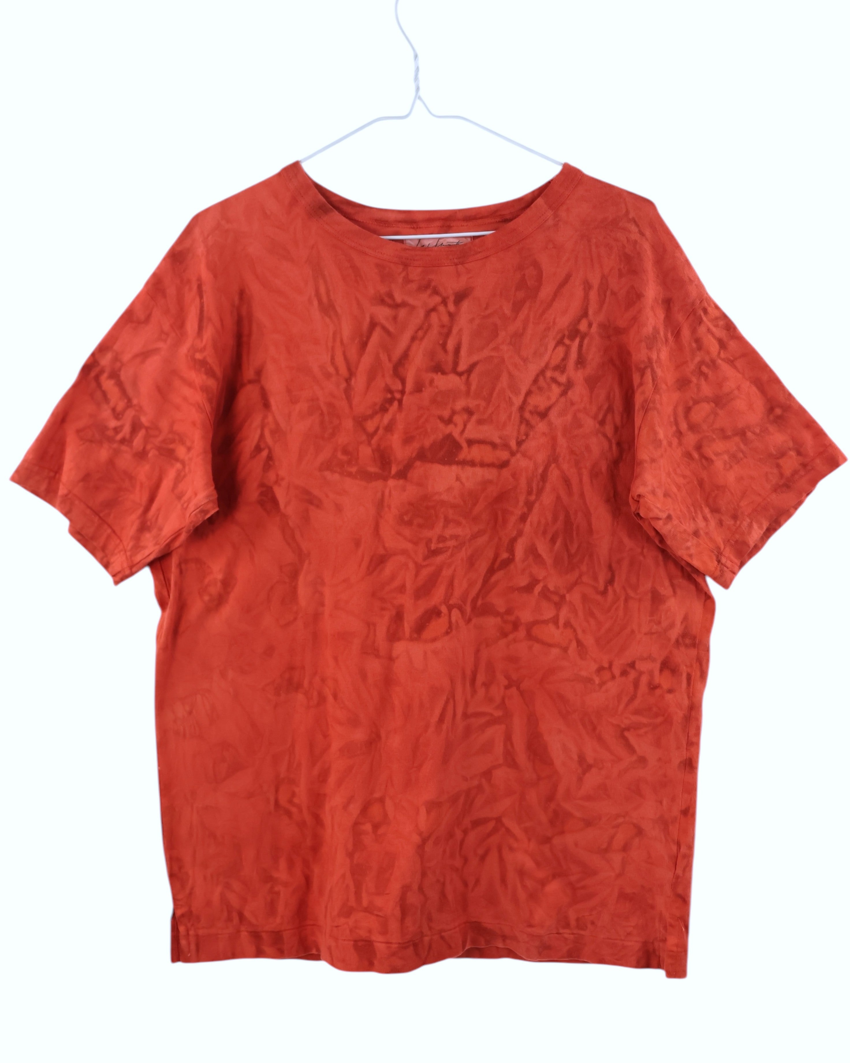 Red t-shirt on a white hanger against a white background. Yohji Yamamoto bold red short-sleeve T-shirt; luxurious silk-blend fabric with distinctive crinkled texture and relaxed oversized silhouette; minimalist neckline and Japanese avant-garde tailoring highlighting artistic imperfection and organic movement; elevated modern essential combining texture, form, and understated luxury.