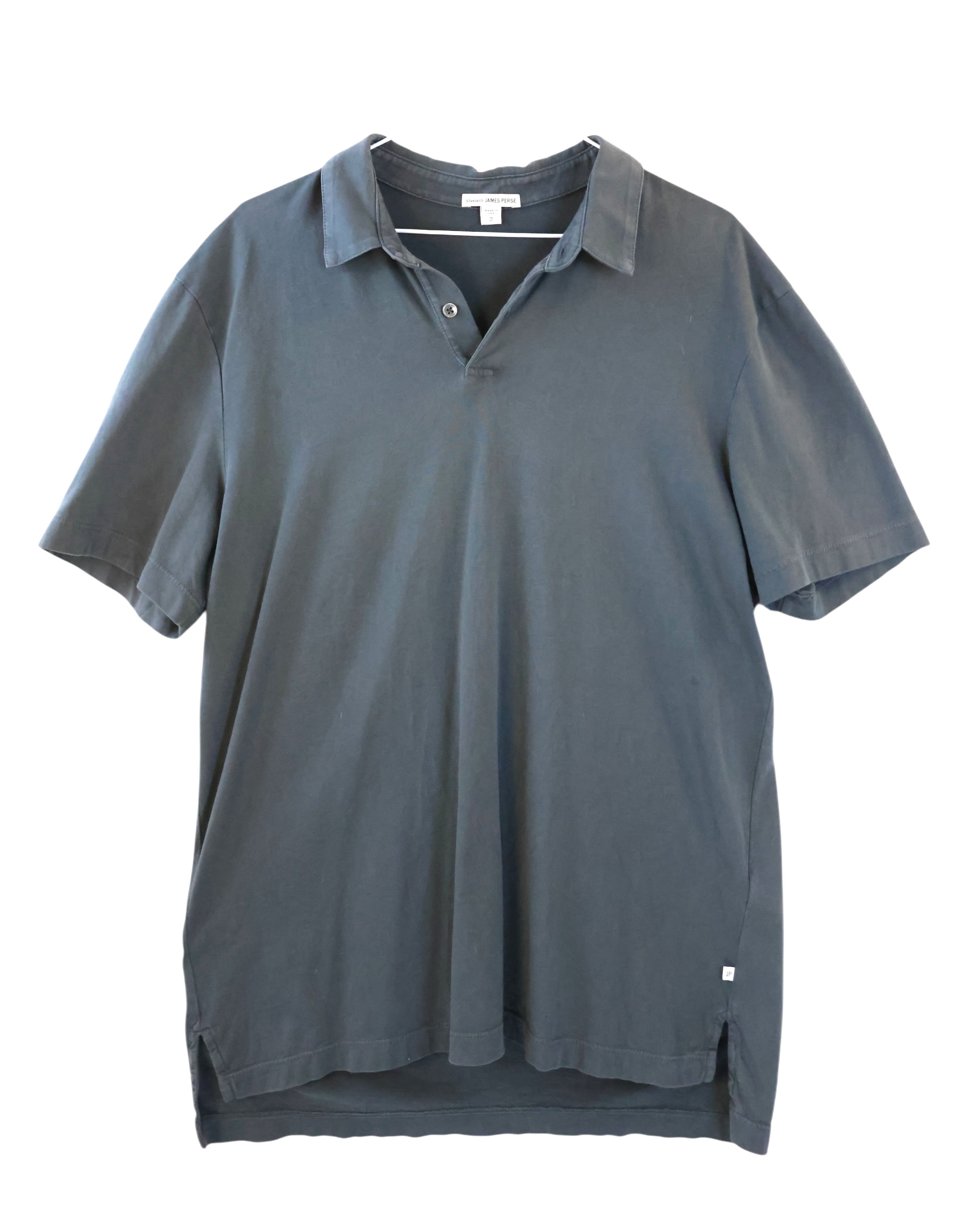 Blue polo shirt on a white background. James Perse slate grey short-sleeve polo shirt; soft washed cotton with open collar and single-button placket; minimalist California-inspired design with relaxed drape and side vents; premium casual essential showcasing effortless luxury and refined comfort in timeless understated style.